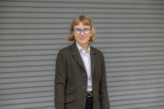 Headshot of a white woman with short blonde hair wearing a gray blazer.