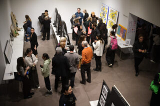 A birds eye view of the Art by Architects showcase installed in a gallery setting with people walking around looking at art