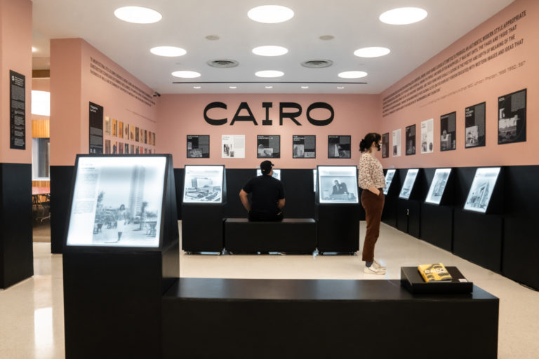 Installation image of black and pink walls with a black bench and lightboxes on the perimeter of the room