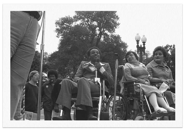 Black-and-white photograph of three people in wheelchairs, including Black Panther Brad Lomax and activist Judy Heumann