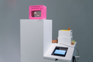 Installation view of a white podium structure that holds an embedded iPad screen and several rectangular objects.