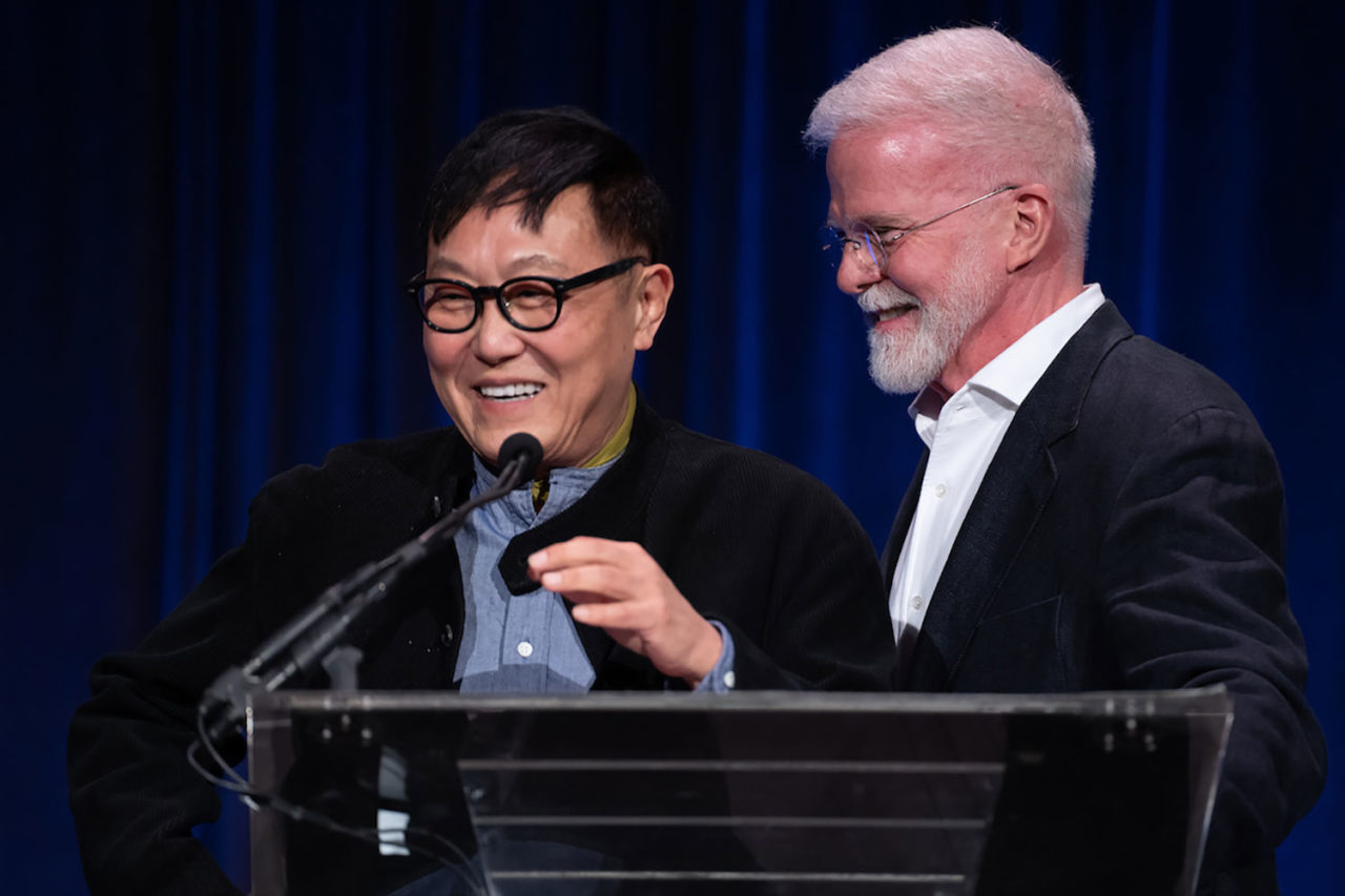 Two men stand over a podium smiling at each other.