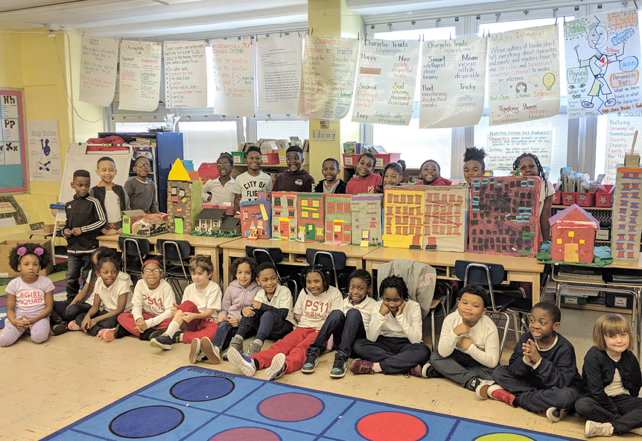 Students in a classroom sitting in front of a table showing models of multi-family housing structures