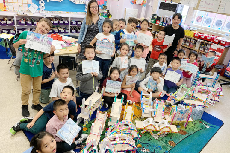 Group of students and a teacher standing in a classroom surrounded by models of bridges