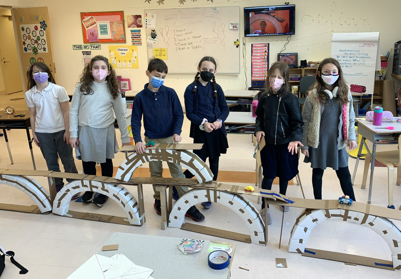 Students stand in front of a model of an arch bridge.