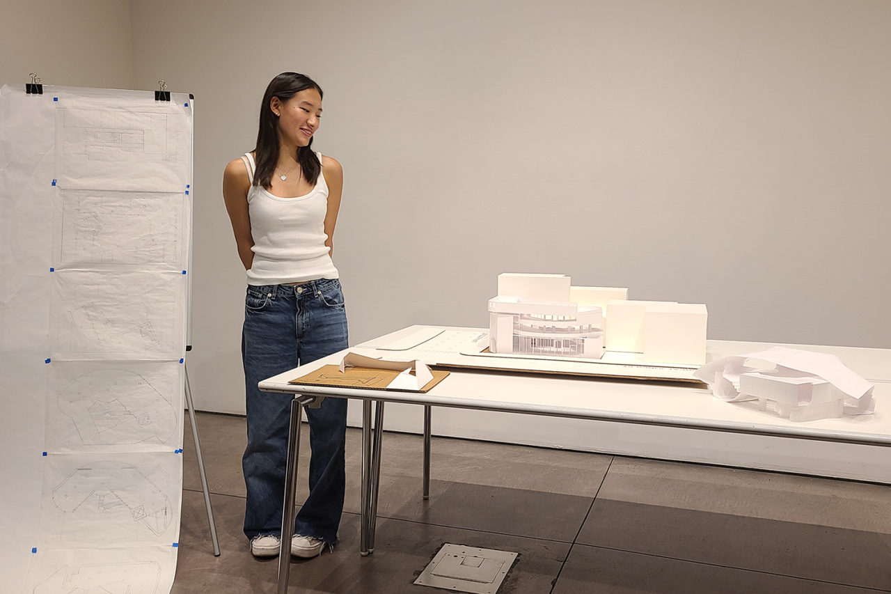 High school student stands next to a white hand-made model.