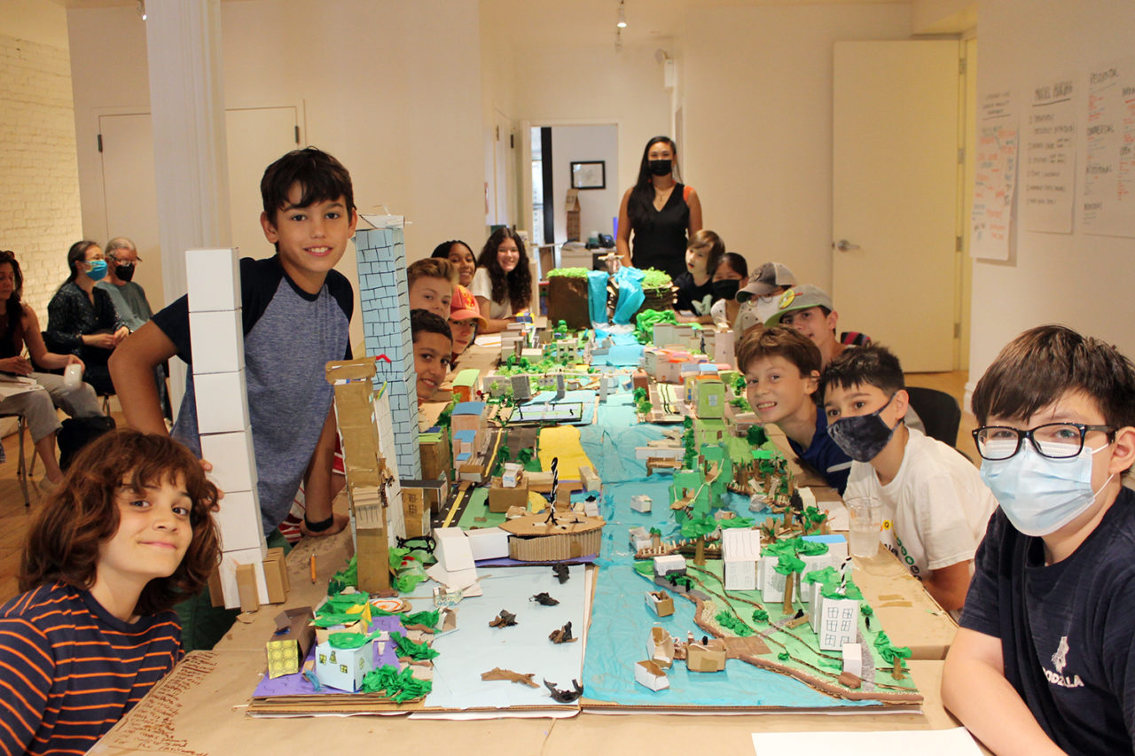 Students sit at a long table covered with models of waterfront cities.