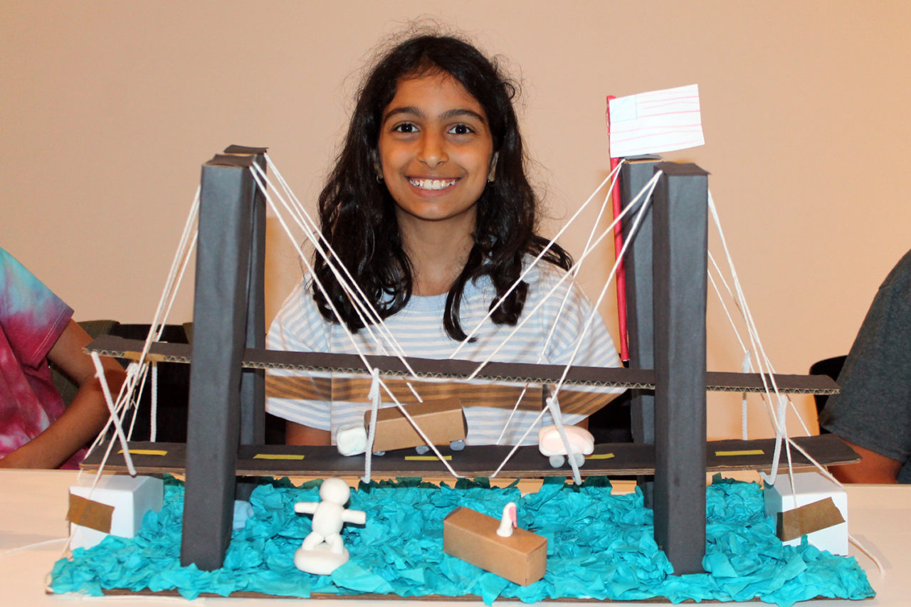 Student sits behind a hand-made model of a bridge.