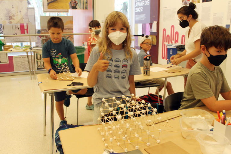 Student stands in front of a toothpick and marshmallow structure.