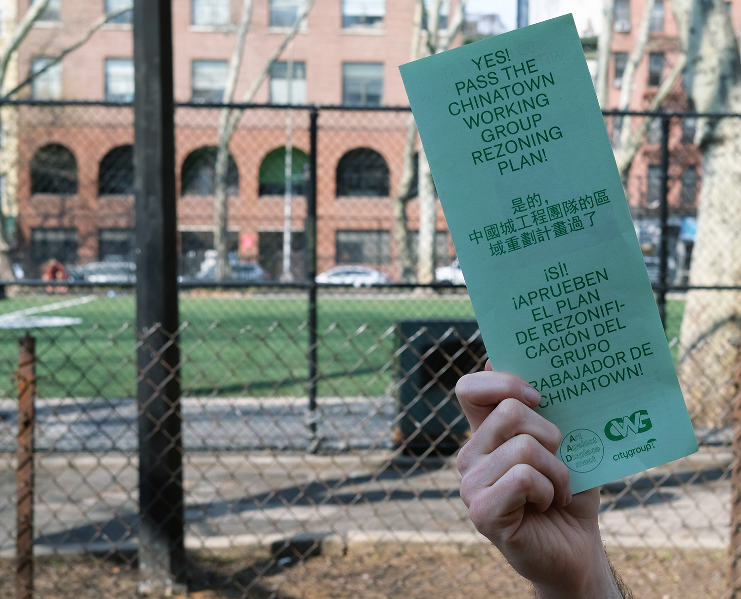 Hand holding a green flyer with text in English, Spanish, and Chinese that reads: Yes! Pass the Chinatown Working Group Rezoning Plan!