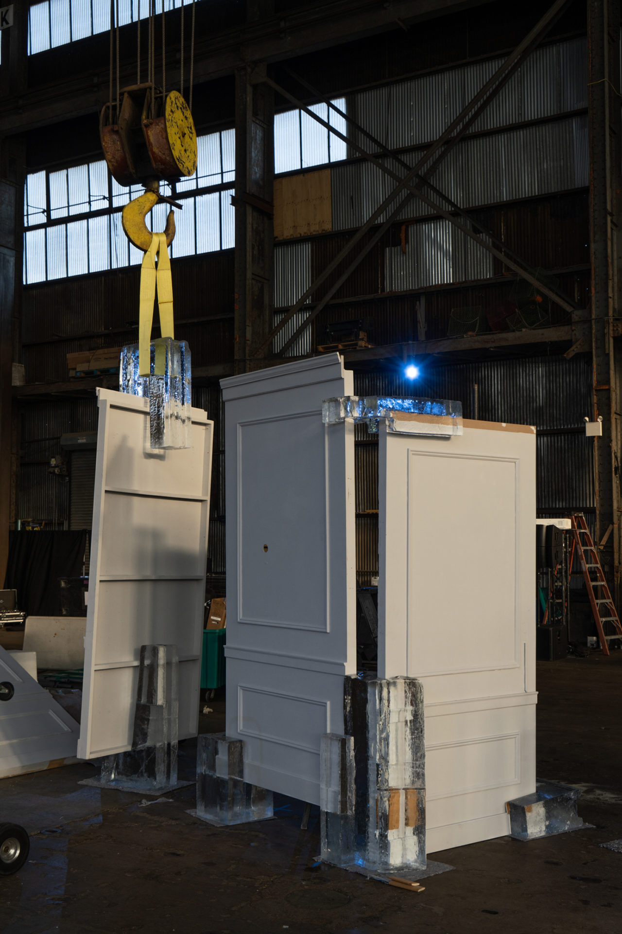 Three panels, one held up by a crane, set into blocks of ice within an industrial interior
