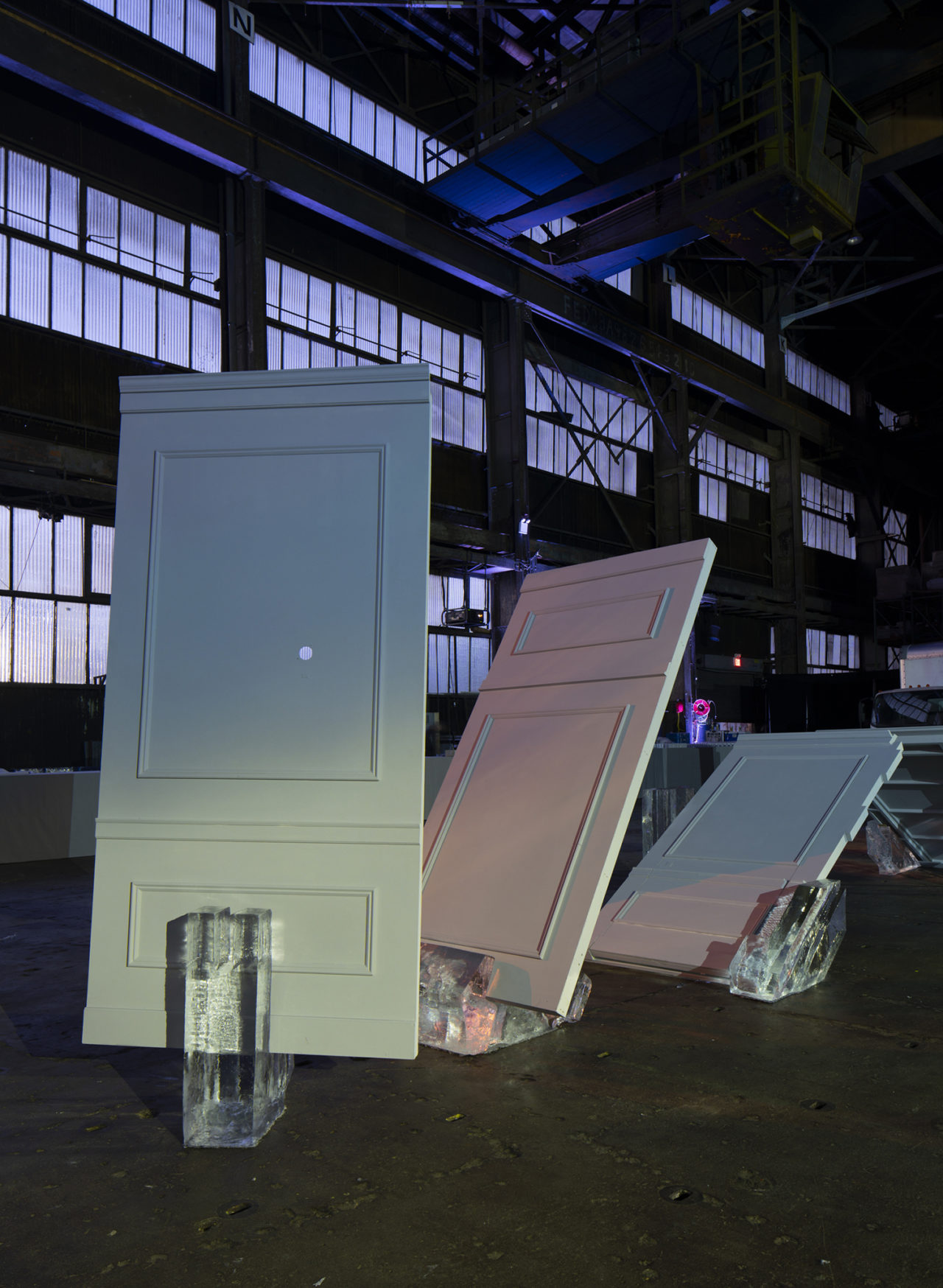 Three panels set into blocks of ice at different degrees of incline within an industrial interior