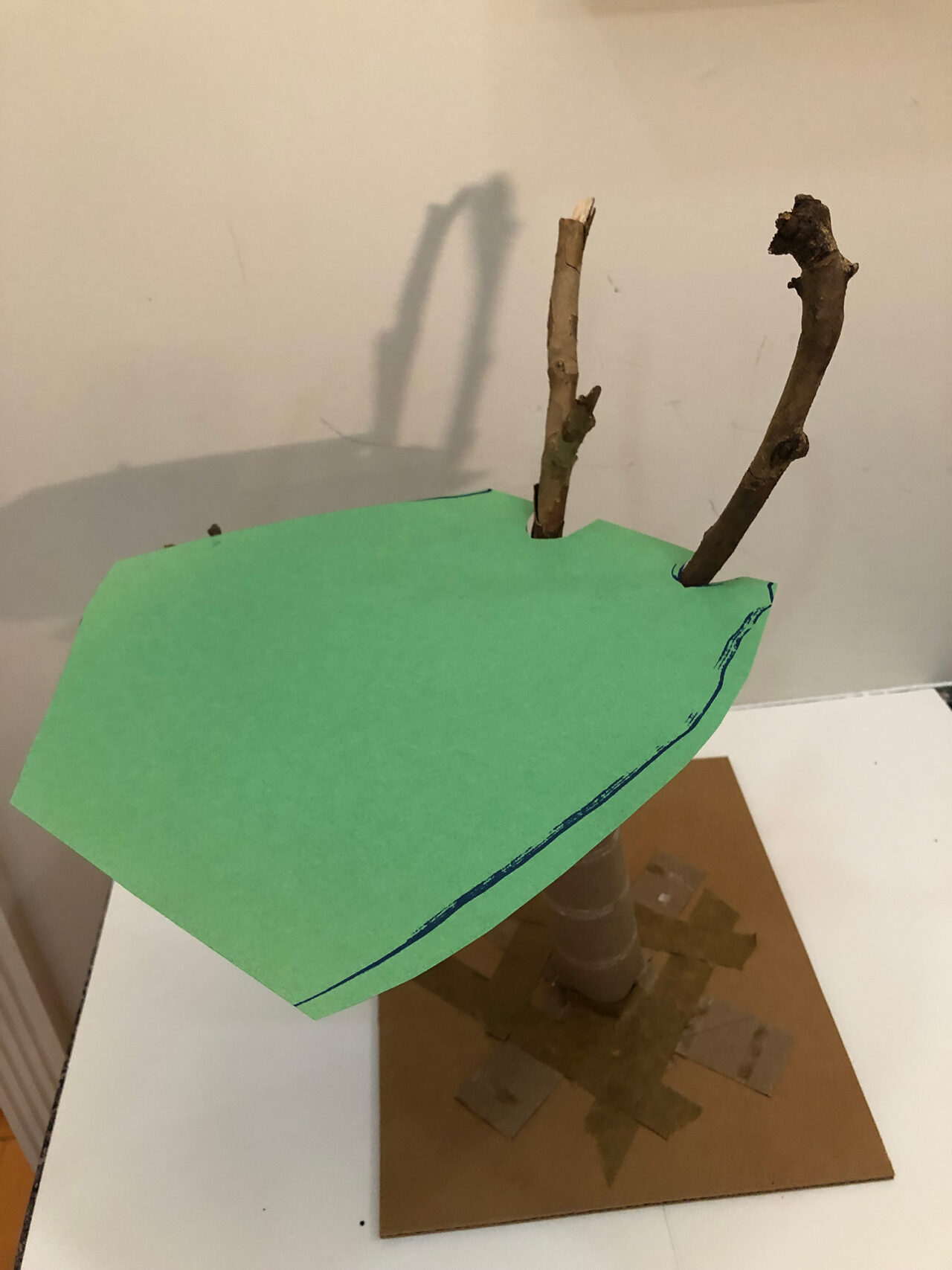 A piece of green construction paper sits atop the branches of the structure.