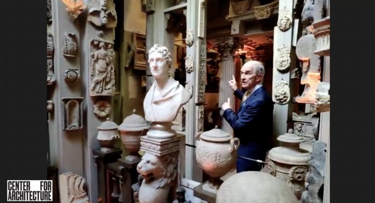 Man pointing to installation of architectural details and female bust sculpture