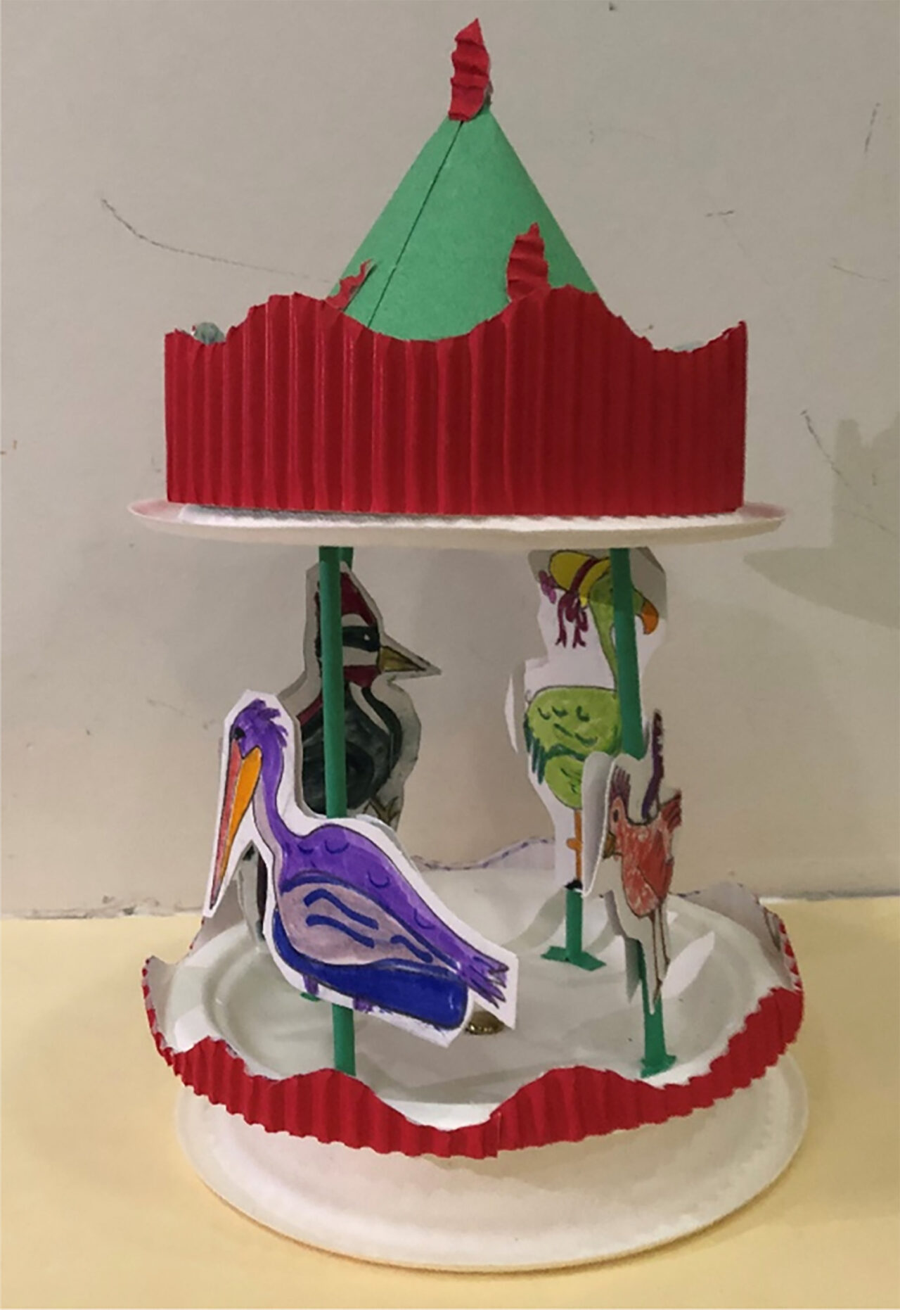 A merry go round made of construction paper and straws. Colorful illustrations of birds are taped to the straws.