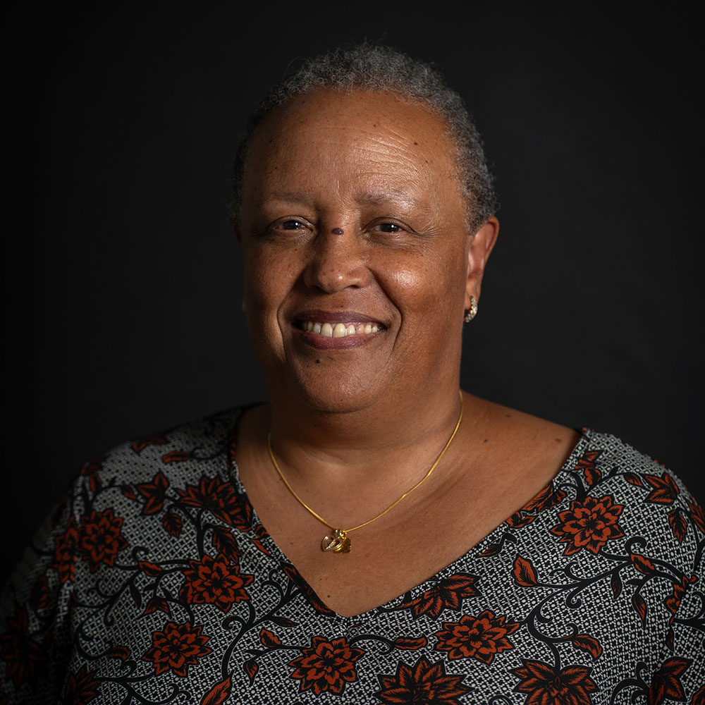 A headshot of a Black woman with short hair, smiling against a black background.