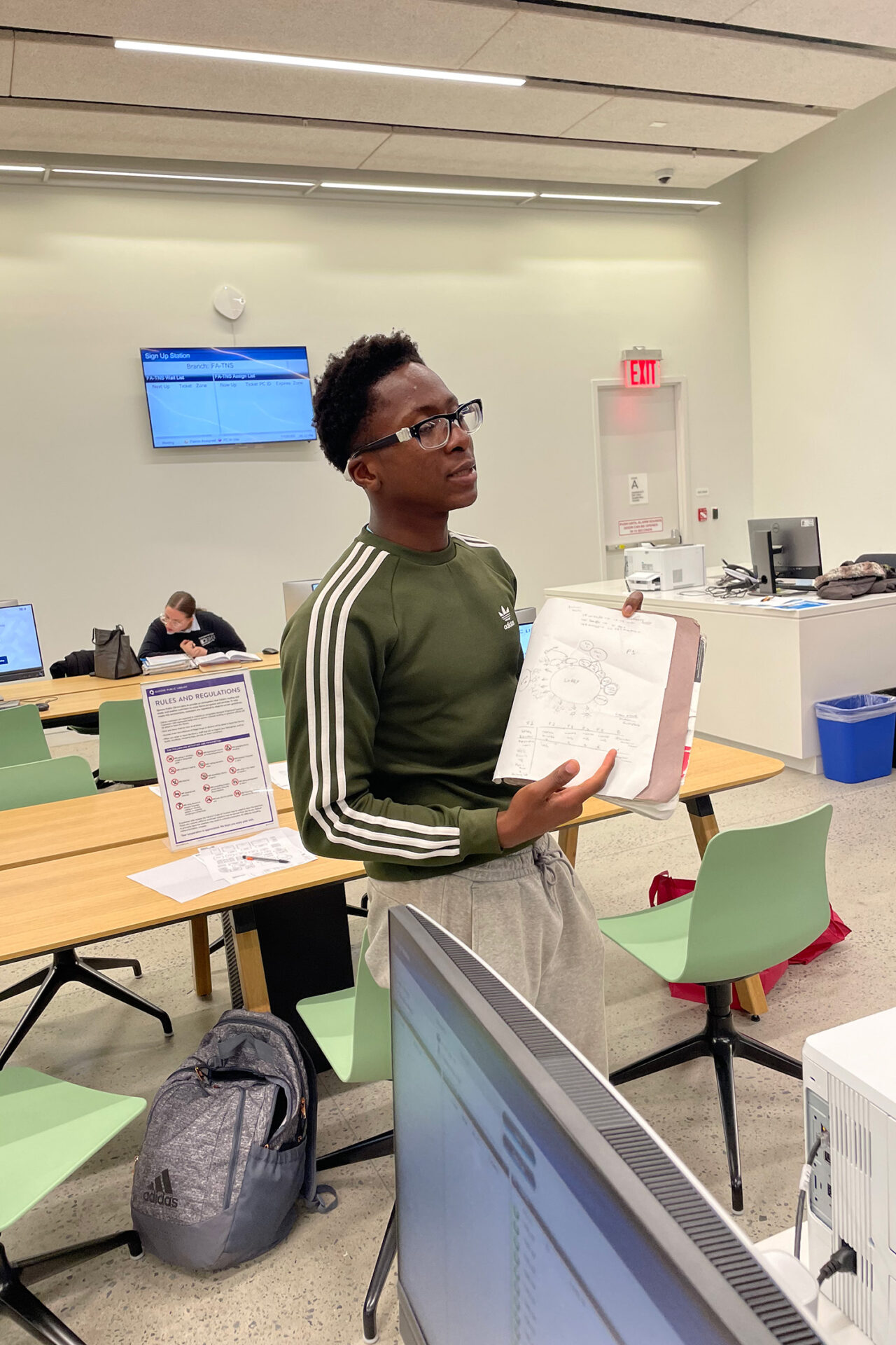 A young student (Black male) holds up a piece of paper in a classroom.