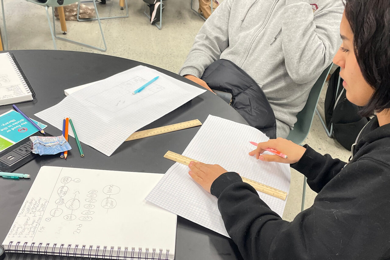 Students sit at a table with graph and notebook paper.