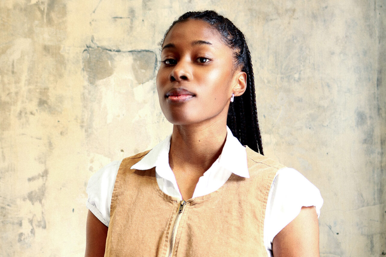 A portrait of a young Black woman against a tan backdrop.
