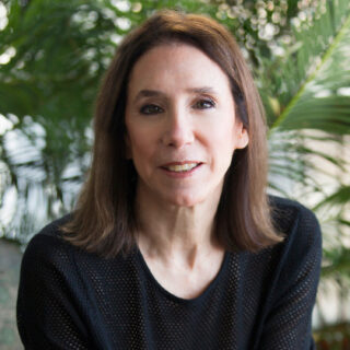 A headshot of a white woman with shoulder-length brown hair in a black long sleeve.