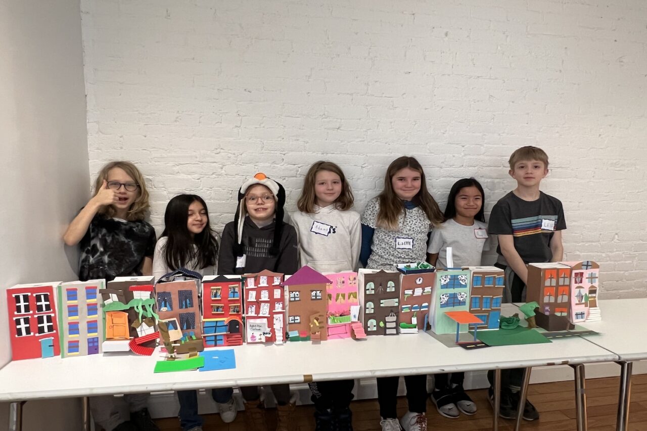 Seven elementary school students standing behind a table displaying their model rowhouses.