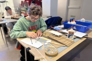 One high school student working on small architectural model made of cardboard and paper.