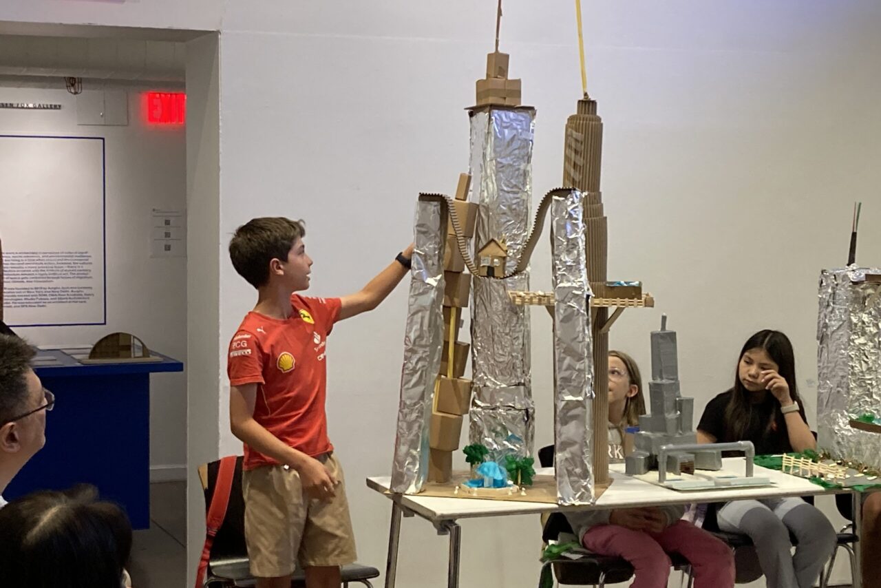 Middle school student standing next to large silver skyscraper model