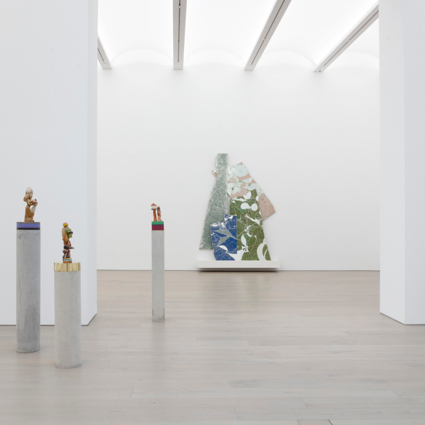 White gallery interior with several sculptures on podiums and a large scale painting in the background