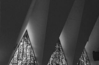 Black and white photo of triangular stained glass reflecting onto vaulted cathedral ceiling.