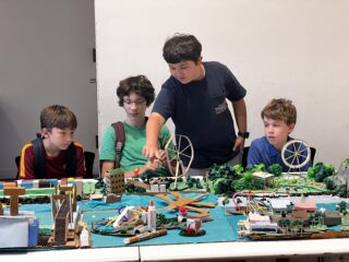 Four middle school students gesturing to model of a waterfront city