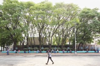 Image of a person walking outdoors with people seated on a blue bench