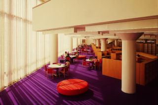 Double height interior and single story mezzanine on top of a purple carpet with tables and office cubicles scattered throughout