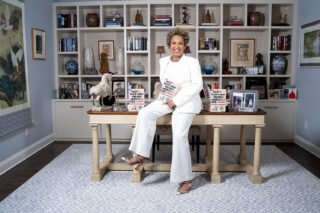 Woman sitting on a desk holding a book in an office